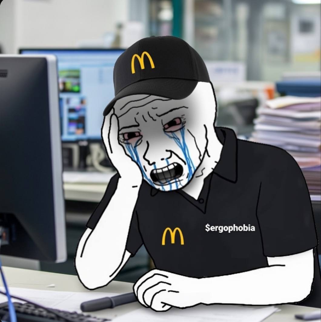 Worker crying at desk with $ergophobia on shirt
